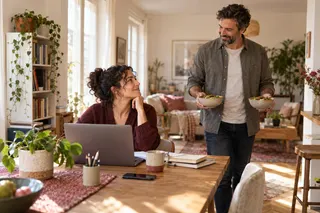 A woman looks up from her laptop as a man brings two bowls of food.