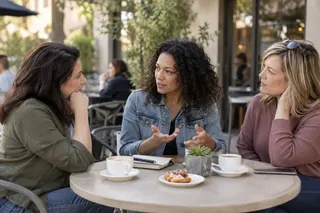 Three women talking together at an outdoor cafe table.