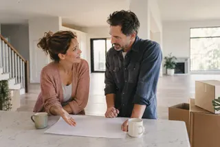 Two adults talking at a kitchen island beside moving boxes.