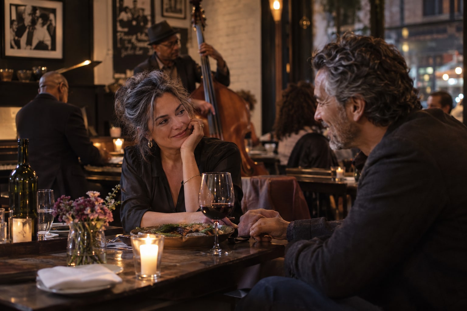 Two adults hold hands across a candlelit restaurant table with live musicians behind them.