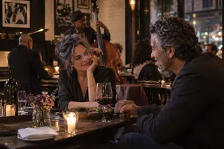 Two adults hold hands across a candlelit restaurant table with live musicians behind them.