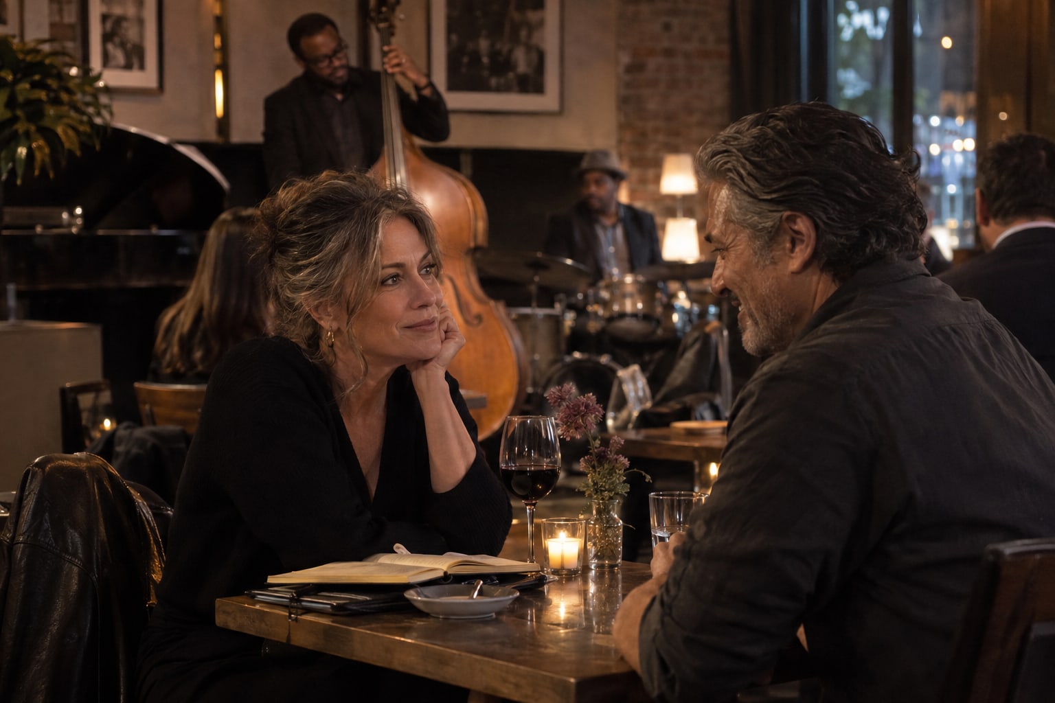Two adults talk across a candlelit table, with an open notebook and musicians nearby.