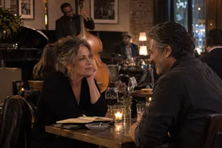 Two adults talk across a candlelit table, with an open notebook and musicians nearby.
