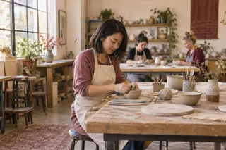 A woman shapes a small clay bowl at a daylight pottery workshop.
