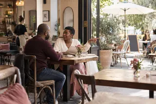 A woman gestures toward outdoor seating while talking with another adult at a cafe.